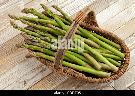 Asparago Verde in cesto in vimini su grunge verniciato bianco sullo sfondo di legno Foto Stock