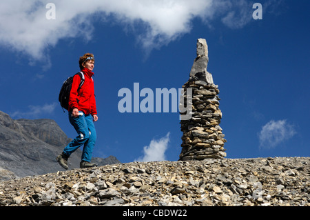 Escursionista passando da un tumulo come segno direzionale e guida di orientamento in un roccioso, trailless area alpina, Vallese Svizzera Foto Stock