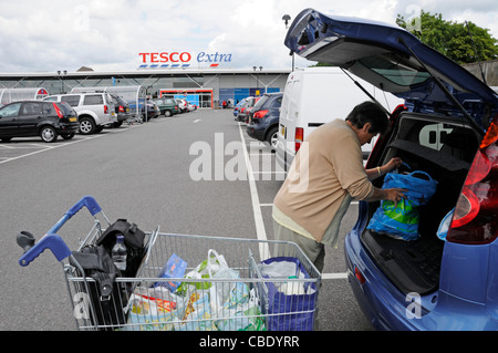 Sessanta nove anni donna senior titolare di pensione o di rendita caricamento settimanale negozio di alimentari da sacchetti di plastica in carrello nel retro della berlina auto presso un supermercato Tesco UK Foto Stock