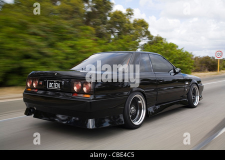 Ripresa posteriore di una degli anni ottanta culto modificati e custom HR31 Nissan Skyline guidando lungo una strada Foto Stock