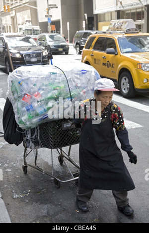 Donna con carrello caricato con bottiglie raccolte da sacchi della spazzatura e lattine in NYC. Foto Stock