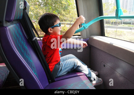 Si tratta di un bambino ragazzo che finge di guidare un autobus con double deck. Egli indossa t-shirt rossa e occhiali da sole. Egli è solo e in jeans. Foto Stock