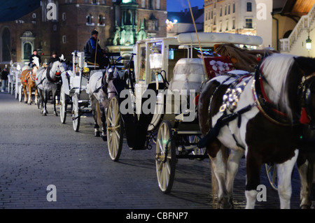 Cavallo e tour turistici linea di carrelli fino a notte in Rynek Glowny, Cracovia Foto Stock