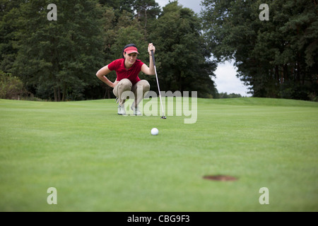 Un giocatore di golf femminile accovacciato studiando la distanza del foro Foto Stock