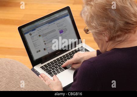 Donna matura usando il suo computer portatile, su internet con una rete sociale sullo schermo. Foto Stock