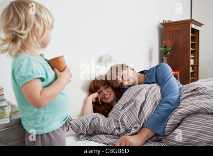 Un giovane che giace nel letto con il loro bambino in piedi accanto al letto Foto Stock