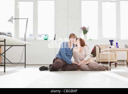 Una giovane coppia affettuoso seduti fianco a fianco sul pavimento Foto Stock