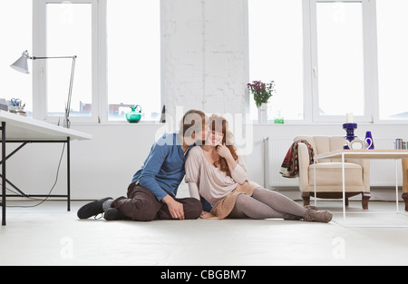 Un giovane uomo di baciare la sua ragazza, fianco a fianco, seduto sul pavimento Foto Stock