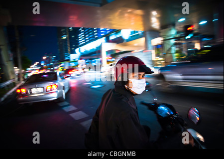 Un uomo indossare una maschera per proteggere se stesso dall'aria inquinata mentre in sella a una motocicletta. Foto Stock