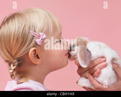 Carino bambina di tre anni baciando un animale da compagnia il coniglio isolato su sfondo rosa Foto Stock