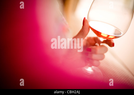 Donna che mantiene un bicchiere di vino rosato. Sun è riflessa dal vetro e vino. Foto Stock