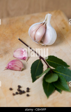 Un rametto di foglie di alloro, pepe nero in grani e aglio su un tagliere di legno. Foto Stock