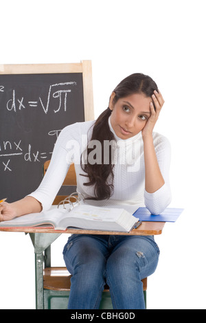 Etnici indiani studente femmina seduto da banco in classe math. Lavagna con formule avanzate è visibile in background Foto Stock