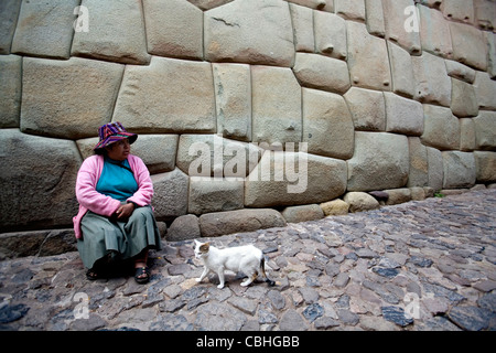 Donna indiana seduto sotto il palazzo di Inca Roca parete laterale in Cusco, Perù Foto Stock