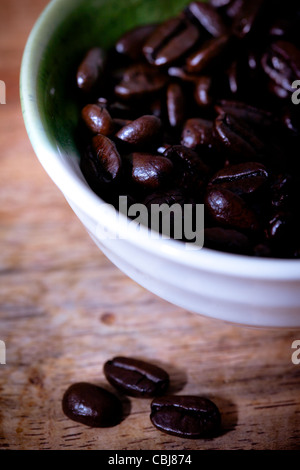 I chicchi di caffè in una ciotola bianco, Sfondo legno Foto Stock