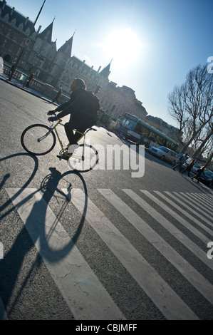 Un uomo che cavalca una bicicletta su una strada principale a Parigi, Francia, mentre il sole forte dietro di lui getta una lunga ombra. Foto Stock