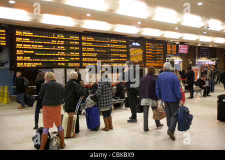 Gente correre passato locale e treni nazionali le schede di informazioni alla stazione ferroviaria di King's Cross Londra Inghilterra Regno Unito Regno Unito Foto Stock