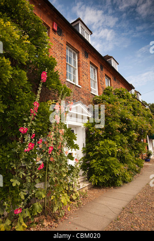 Regno Unito, Inghilterra, Bedfordshire, Woburn, Leighton Street, hollyhocks crescente al di fuori di casa nel piccolo giardino anteriore Foto Stock