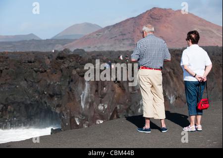 Turisti che visitano Los Hervideros (i bollenti), attrazione turistica naturale sulla costa dove i flussi lavici del vulcano solidificato sono stati erosi dall'oceano Atlantico, con wave.induced geyser, versamenti e nebbia, Lanzarote, Canarie, Spagna. Foto Stock