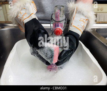 La donna vestita di nero Guanti di gomma lavaggio fino una bottiglia di vetro in Inghilterra Foto Stock