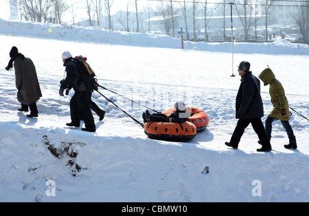 Tirando i ragazzi attraverso la neve in galleggianti gonfiabili, Harbin, Cina Foto Stock