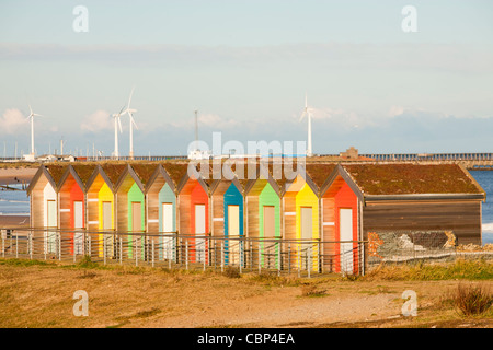 I tradizionali colorati British seaside beach capanne sulla spiaggia di Blyth, nel nord-est, UK, con turbine eoliche dietro. Foto Stock