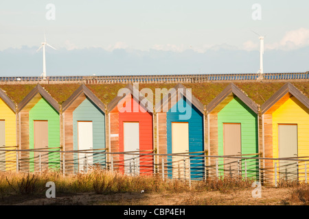 I tradizionali colorati British seaside beach capanne sulla spiaggia di Blyth, nel nord-est, UK, con turbine eoliche dietro. Foto Stock