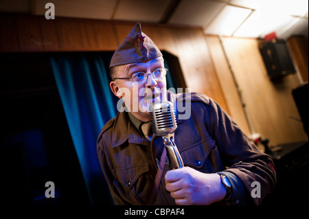 Un presentatore MC vestito come un soldato GI parlando parlando in un microfono a un retro 40s 50s music club, REGNO UNITO Foto Stock