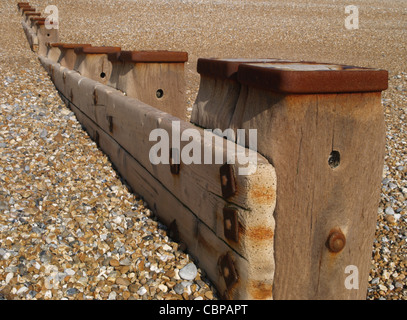 Guardando lungo una struttura di frangionde con posti in fila sulla spiaggia sassosa che guarda lontano dal mare Foto Stock