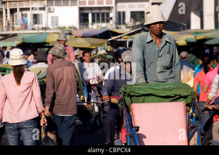 Un driver cyclo è in cerca di clienti mentre pedala su una strada trafficata in Phnom Penh Cambogia. Foto Stock