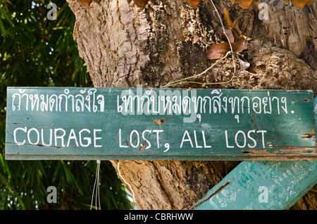 Dipinto a mano segno inchiodato sul tronco di albero dicendo "coraggio perso, tutte perdute' in un tempio buddista in Lamphun Thailandia Foto Stock