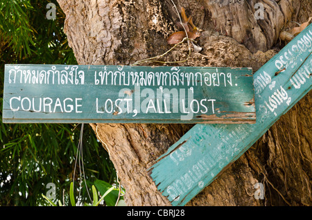 Dipinto a mano segno inchiodato sul tronco di albero dicendo "coraggio perso, tutte perdute' in un tempio buddista in Lamphun Thailandia Foto Stock