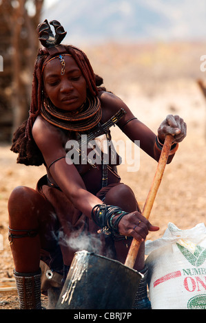 Donna Himba cucinare il loro principale cibo fatto con farina di grano nel suo villaggio vicino a Epupa Falls, regione di Kunene, Namibia settentrionale Foto Stock