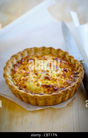 Poco Quiche Lorraine (il formaggio e la cipolla crostata) su arricciata carta oleata con coltello Foto Stock