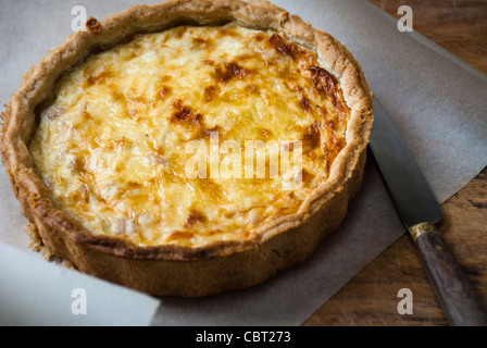 Poco Quiche Lorraine (il formaggio e la cipolla crostata) su arricciata carta oleata con coltello Foto Stock