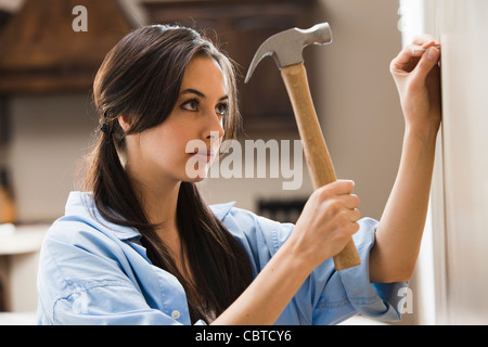 La donna caucasica martellamento chiodo nella parete Foto Stock