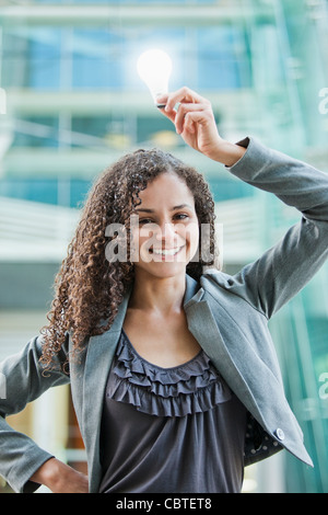 Imprenditrice caucasica holding incandescente lampadina sopra la testa Foto Stock