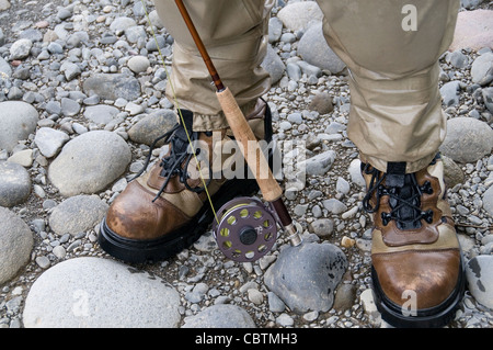 Un pescatore a mosca prepara il suo wading ingranaggio/stivali e asta/aspo per la cattura di Rainbow e la trota marrone su una piccola Nuova Zelanda stream. Foto Stock