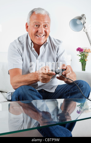 Felice l'uomo senior di riproduzione di video gioco a casa Foto Stock