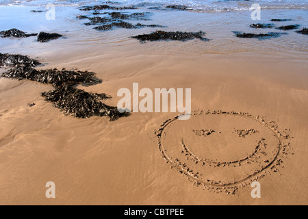 Un'icona raffigurante una faccia sorridente inscritto sulla spiaggia con onde in background su una calda giornata di sole Foto Stock