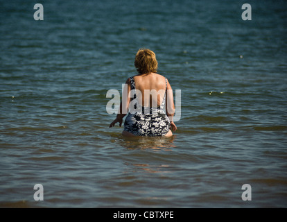 Vista posteriore di una donna caucasica bionda in piedi nel mare a Filey. North Yorkshire. REGNO UNITO Foto Stock