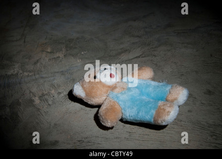 Abuso di minori Concetto di immagine di un bambino orsacchiotto giacente su teh pavimento di una stanza in calcestruzzo Foto Stock