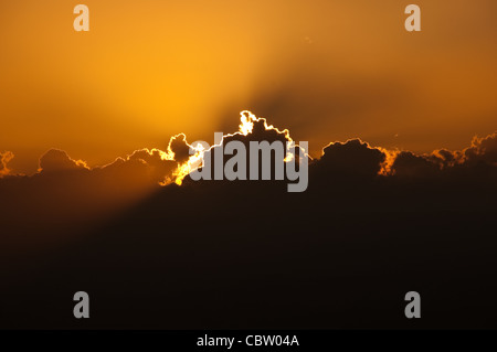 Tramonto dietro big cloud creazione di bagliore arancione nel cielo Foto Stock