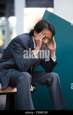 Business uomo seduto sul banco di prova all'aperto non sentirsi bene Foto Stock