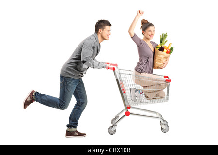 Persona spingendo una donna felice in un carrello della spesa con sacchetto pieno con il cibo Foto Stock