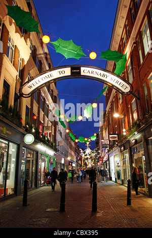 Luci e decorazioni natalizie decorato come agrifoglio e vischio in Carnaby Street a Londra Foto Stock