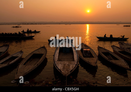 Un sunrise guardando oltre il più sacro dei fiumi in India. Il Gange. Sagome di barche di colline punteggiano l'orizzonte. Foto Stock