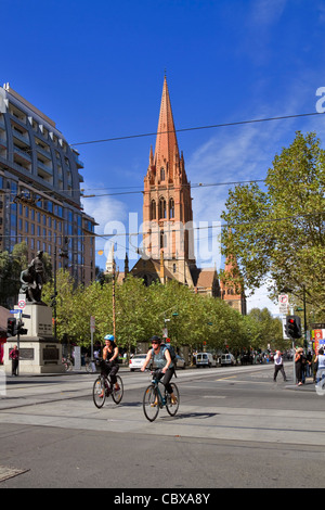 Intersezione di Collins e Swanston strade, Melbourne. I ciclisti guidare su strade trafficate con St Pauls Cathedral in background Foto Stock