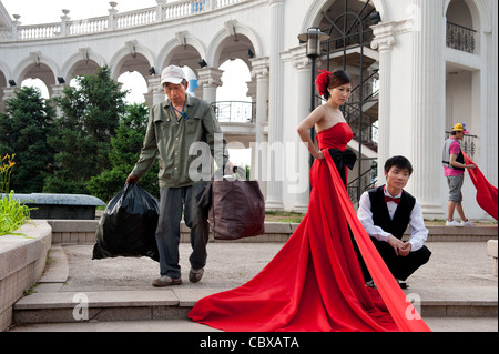Beijing Chaoyang Park. Lavoratore che trasportano rifiuti passando un wedding photo shoot. Foto Stock