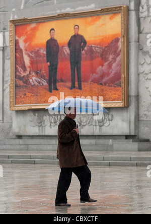 Uomo con un ombrello davanti a un poster di propaganda, Pyongyang, Corea del Nord Foto Stock